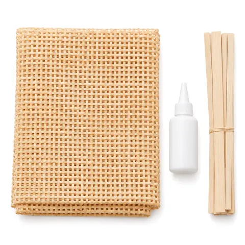 Flat lay of a folded square weave cane sheet, a plain glue bottle and thin pine trim strips on blush pink paper, on a white background
