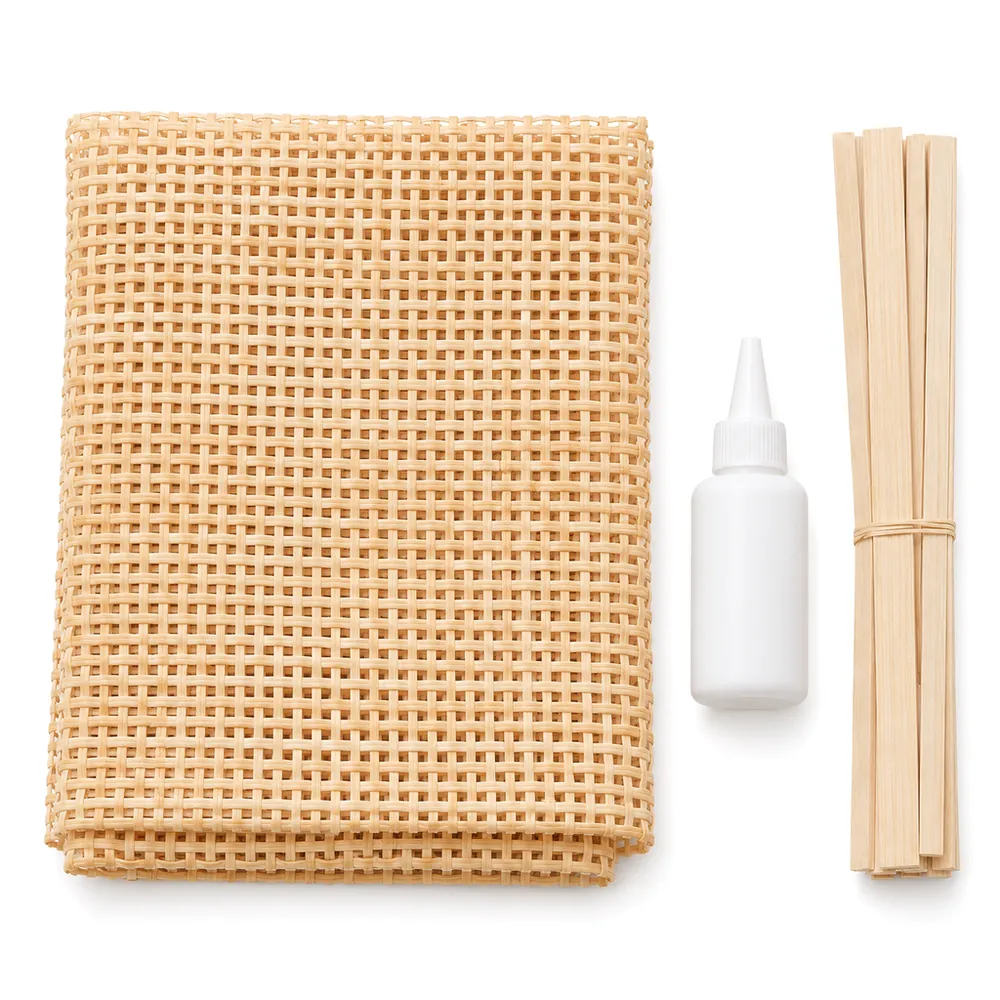 Flat lay of a folded square weave cane sheet, a plain glue bottle and thin pine trim strips on blush pink paper, on a white background