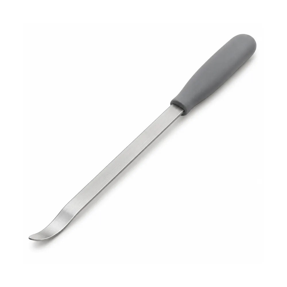 Flat stainless steel wicker tool with a slim curved tip and grey silicone handle, lying diagonally on terracotta, on a white background