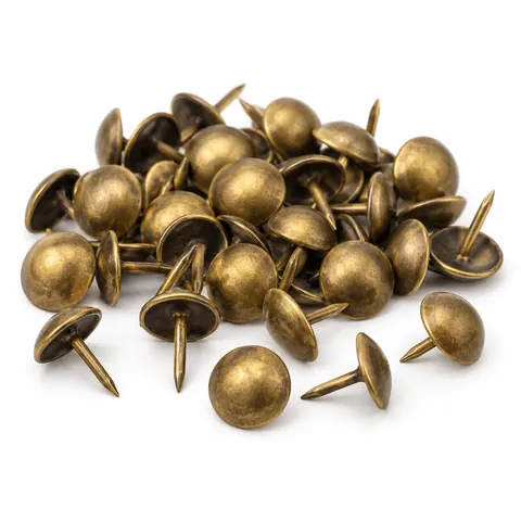 Small pile of antique brass domed upholstery tacks, a few apart showing their pointed shanks, on a white background