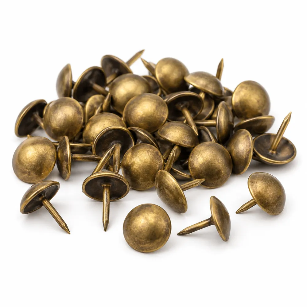 Small pile of antique brass domed upholstery tacks, a few apart showing their pointed shanks, on a white background