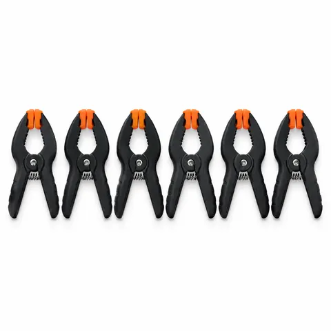 Row of six small black and orange plastic spring clamps with padded tips, on a white background