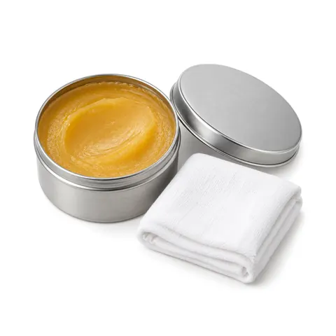 Open tin of honey-colored paste wax with its lid beside it and a folded white cotton cloth, on a white background