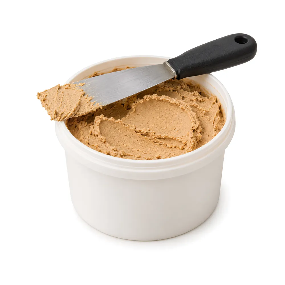 Open tub of tan wood filler with a small metal putty knife resting on the rim, on a white background
